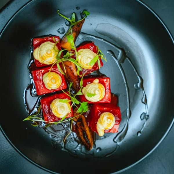 Chicatana's red square appetizers topped with yellow cream and green garnish on a black plate.