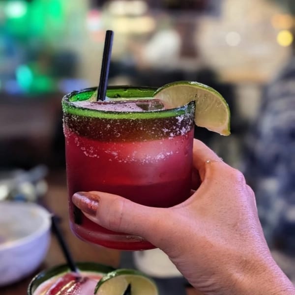 A hand holding a vibrant red margarita with a green salted rim and lime wedge.