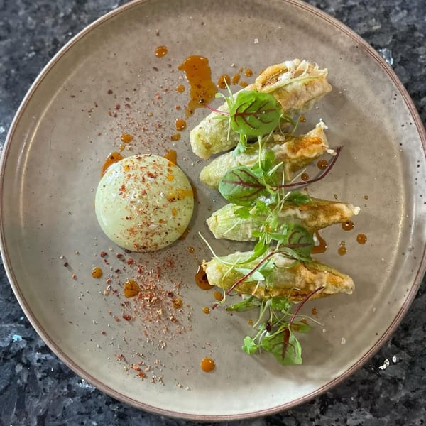 Chicatana's fried zucchini blossoms with a green sauce and chili flakes on a rustic plate.