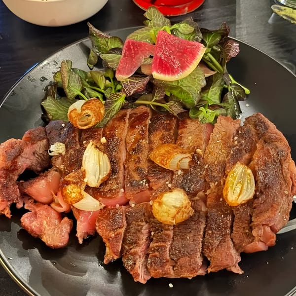 Chicatana's sliced steak with roasted garlic, fresh greens, and watermelon radish on a black plate.