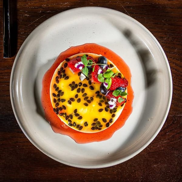 Chicatana's passion fruit dessert with berries, edible flowers, and a red sauce on a white plate.
