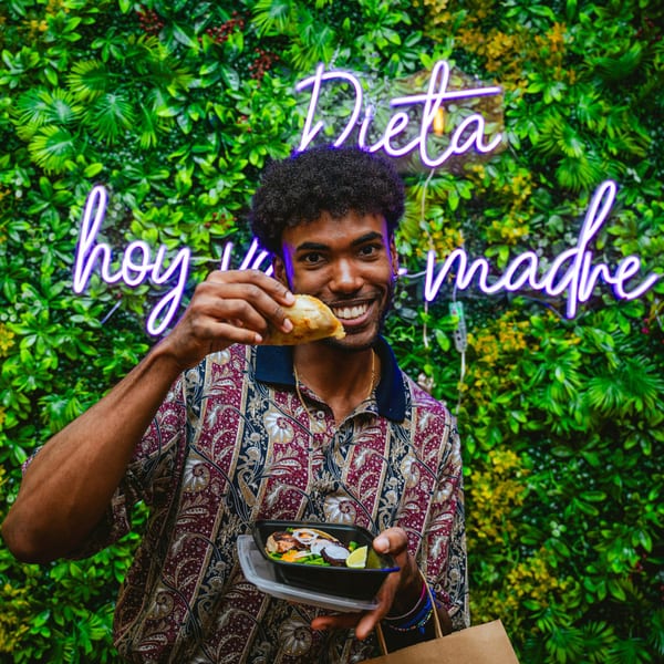 Smiling man holding a Chicatana Mexican empanada and a to-go container with food.
